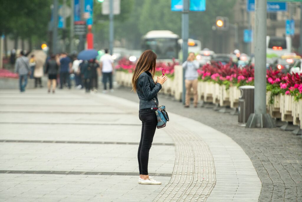 Woman checking her smartphone on a busy city sidewalk, the distracted-walking habit Android's Heads Up feature was built to curb