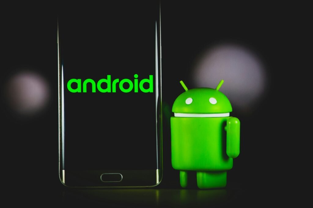 A green Android robot figurine standing next to a smartphone, representing Google's Android 18 release teased for the Android Dev Summit