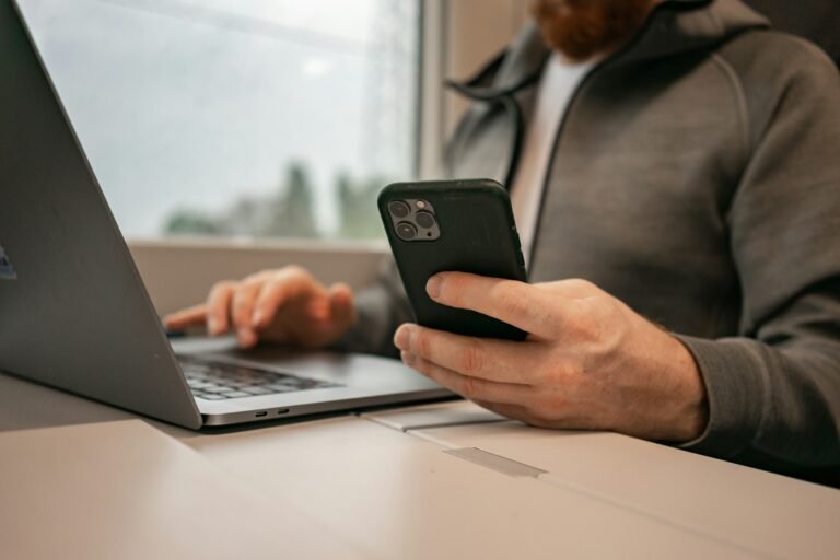 Hands typing on a laptop while holding a phone, representing using Gemini 4 Argon for chat and coding tasks