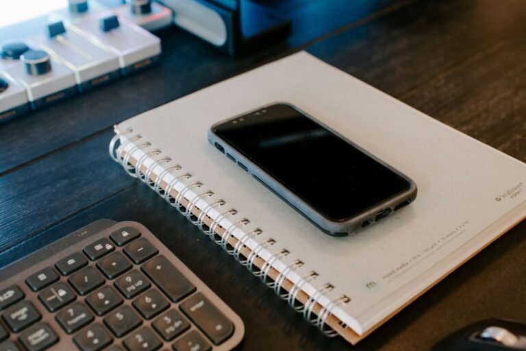 A phone resting on a paper notebook next to a keyboard, a work-and-personal scheduling setup that Google Calendar's per-calendar defaults target