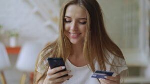 A woman shopping online on her smartphone with a card in hand, illustrating Google's Universal Cart in Search and Gemini