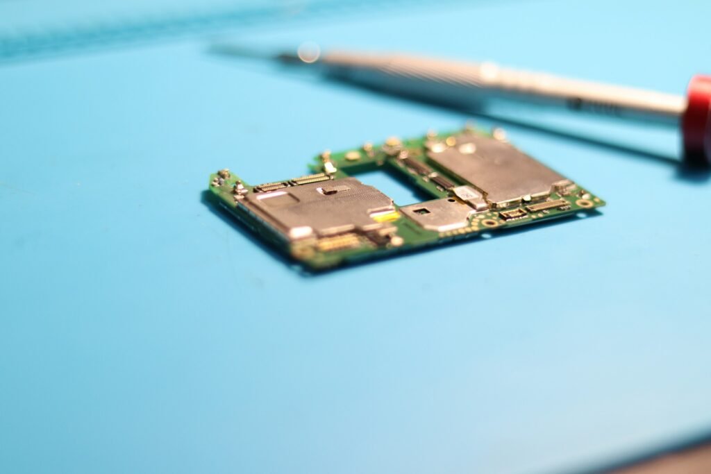A smartphone circuit board with memory and processor chips beside a screwdriver, illustrating rising component costs behind Samsung's production cuts